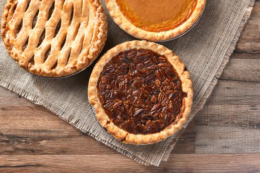 Three fresh baked Thanksgiving Pies. A Pecan Pie, Apple pie and Pumpkin pie seen from a high angle on a burlap and wood surface.