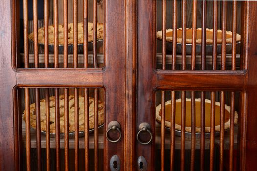 Closeup of an old fashioned pie safe with pumpkin and apple pies behind the doors. Four fresh baked holiday pies on two shelves of the wooden cooling cabinet. Horizontal filling the frame.