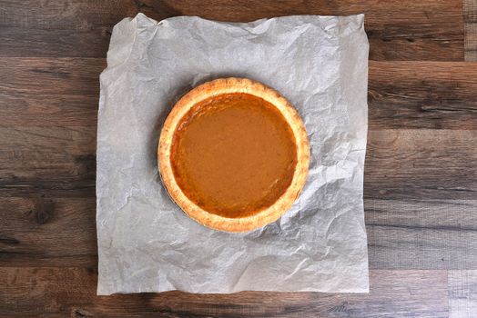 Overhead view of a whole pumpkin pie on parchment paper and dark wood table.