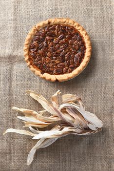 Vertical high angle view of a pecan pie on burlap with corn husks.