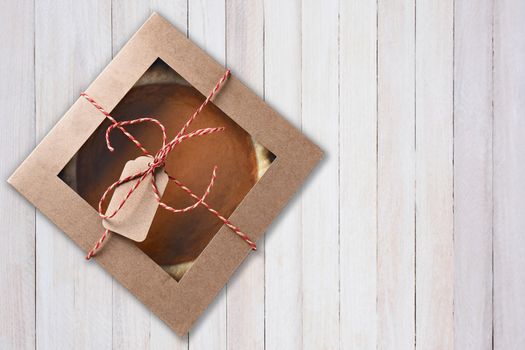 Fresh pumpkin pie in a bakery box tied with string and a blank tag. High angle view on a white wood table