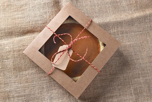 Fresh pumpkin pie in a bakery box tied with string and a blank tag. High angle view on a burlap surface.