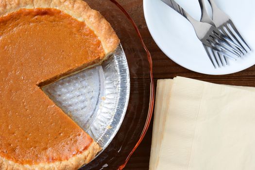 Overhead view of a holiday pumpkin pie with a slice cut out. Horizontal format with napkins, plate and forks.