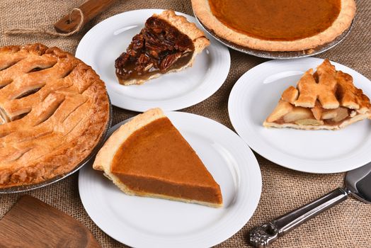 High angle view of whole pies and plates with slices. Traditional Thanksgiving desserts include, Pecan Pie, Apple Pie and Pumpkin Pie.