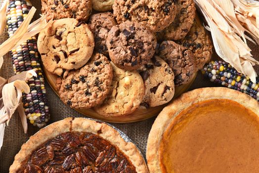 Closeup of pies and cookies for a Thanksgiving Day feast desserts. Pecan Pie, Pumpkin Pie, Chocolate Chip, oatmeal raisin and indian corn adorn the table.