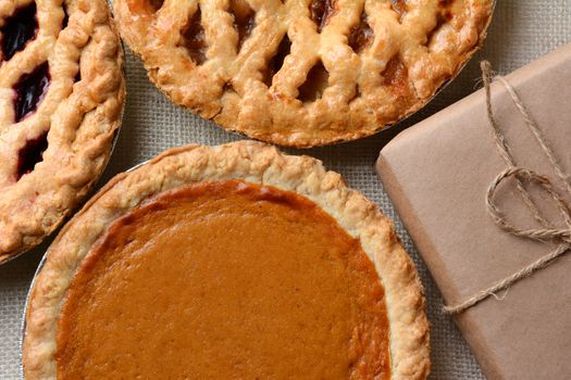 High angle closeup of three fresh baked holiday pies and a plain paper wrapped package. The traditional anerican desserts - Pumpkin, Cherry and Apple pie are Thanksgiving staples. Horizontal format.