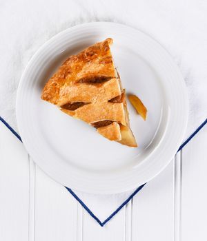 High angle view of a fresh baked apple pie slice on a white plate and kitchen towel.