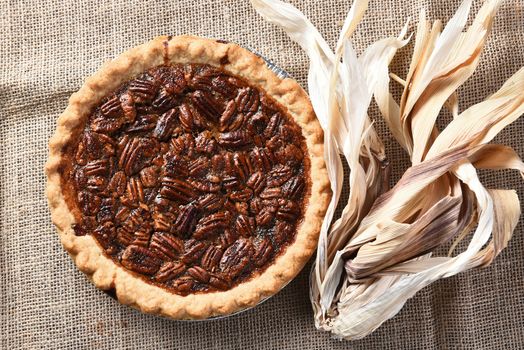 Horizontal high angle view of a pecan pie on burlap with corn husks.