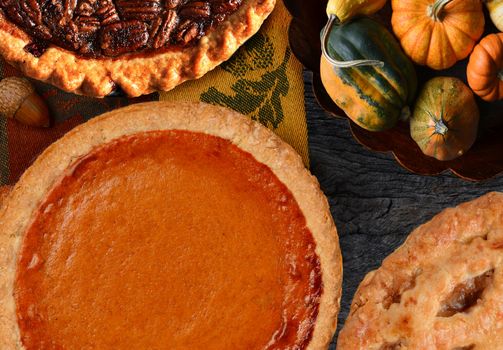 Thanksgiving Holiday Pumpkin, Apple, and Pecan Pies on a rustic table with decorative gourds.