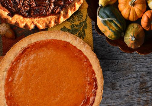 Overhead view of a fresh baked pumpkin pie ready for Thanksgiving. The pie is surrounded by autumn accessories including acorns, and mini pumpkins. Horizontal format.