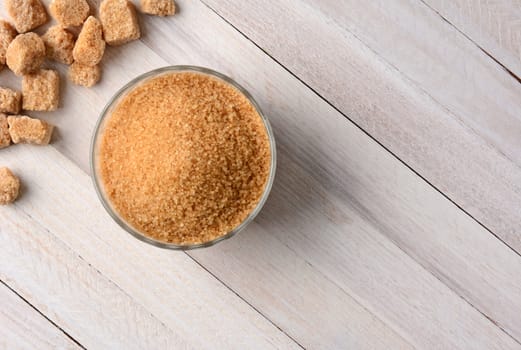 Overhead view of chunks of raw brown sugar and a bowl full of trubinado granules on a white wood table.