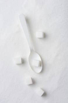 Overhead view of a white spoon, sugar cubes and granulated sugar.