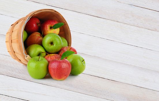 High angle shot of a basket full of Gala and Granny Smith apples spilling out onto a rustic wood surface.