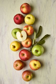 A group of different varieties of apples with leaves on a rustic table. Vertical format viewed from a high angle.