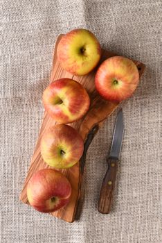 High angle view of a group of Braeburn apples on a cutting board, with a knife on a burlap table cloth.