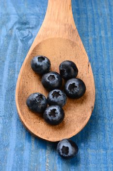 Closeup of fresh blueberries on a wooden spoon laying on a rustic painted farmhouse style kitchen table. Vertical format with shallow depth of field.