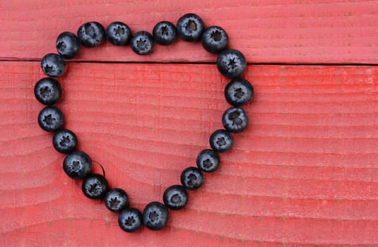 The shape of a heart on a red wood background made from blueberries. Horizontal format with copy space.