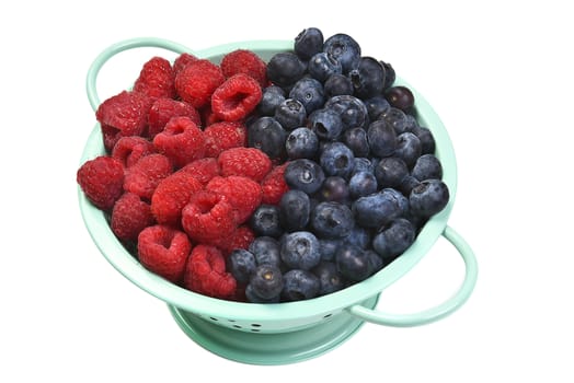 Top view of a colander filled with blueberries and raspberries, isolated on white.