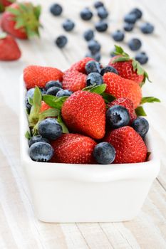 A bowl full of strawberries and blueberries on a rustic farmhouse style kitchen table. Vertical format with shallow depth of field.