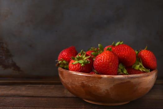 Horizontal still life of a bowl full of fresh picked strawberries on a wood table. Horizontal format with copy space.