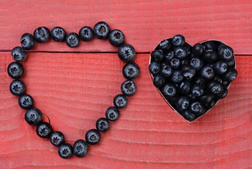 Two different heart shapes made from blueberries on a red wood background.