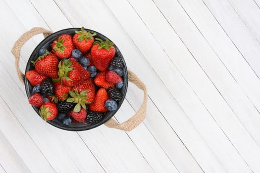 High angle shot of a bucket of fresh picked berries on a rustic whitewashed wood table. The pail is set to the left side leaving copy space.