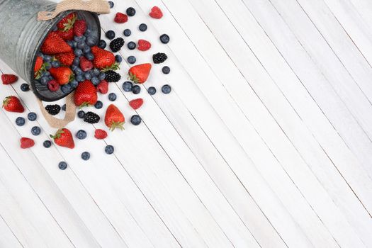 A bucket of berries spilling onto a rustic white kitchen table. High angle shot with the pail in the upper left corner leaving room for your copy.