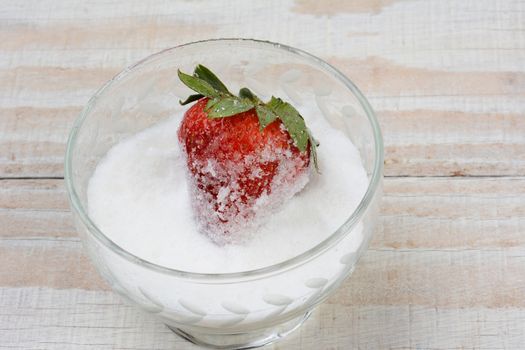 Closeup of a fresh ripe strawberry in a bowl of sugar. The berry is partially covered with granules.