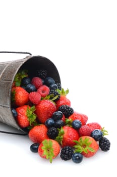 A pail laying on its side with assorted berries spilling out. Vertical format with copy space.