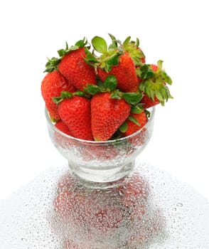 Closeup of fresh picked strawberries in a glass bowl with reflection on a wet surface over a white background.