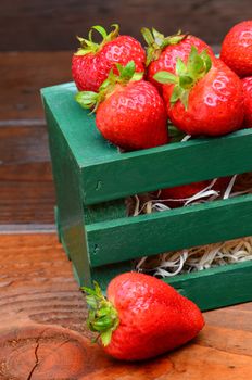 Fresh ripe strawberries in a green wood crate on a rustic wooden background.