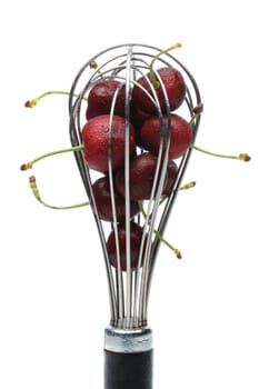A metal whisk filled with fresh ripe cherries. Vertical format on white.