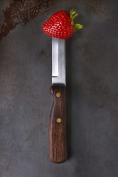 Still life of a fresh picked strawberry stuck on the end of a knife.