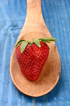 Closeup of a fresh picked strawberry on a wooden spoon laying on a rustic painted farmhouse style kitchen table. Vertical format with shallow depth of field.