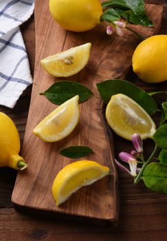 Still life of a group of lemons, whole and cut, on a cutting board. Leaves and lemon flowers and kitchen towel in vertical format.