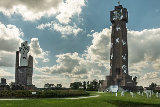 Diksmuide, Flanders, Belgium - September 15, 2018: Tallest peace monument in Flanders, called IJzertoren. brown bricks, white figures, blue sky with clouds, green lawn and PAX crypt.