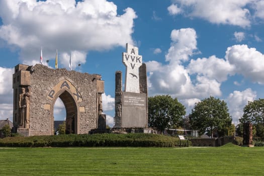 Diksmuide, Flanders, Belgium - September 15, 2018: PAX Gate and crypt ruin at IJzertoren plain. Gray and brown stones, AVV-VVK symbol on white cross, Green lawn with dark green trees under blue sky with white clouds.