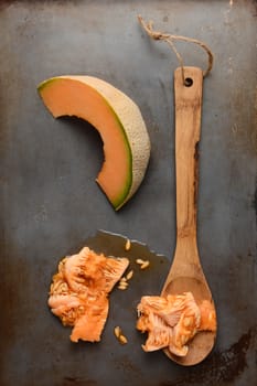 High angle shot of a cantaloupe slice next to a wooden spoon and the seed pulp. Overhead view in vertical format.