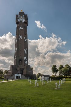 Diksmuide, Flanders, Belgium - September 15, 2018: Tallest peace monument in Flanders, called IJzertoren. brown bricks, white figures, blue sky with clouds, green lawn.