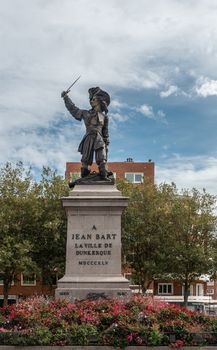 Dunkerque, France - September 16, 2018: Jean Bart, famous Pirate, on his square in Dunkirk with red flowers in front under blue sky with white clouds. Green tree background.