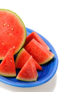 Closeup of a seedless watermelon on a blue platter. Half a melon surrounded by wedges of fruit. Vertical format on a white background with reflection.