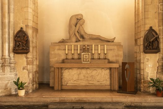 Dunkerque, France - September 16, 2018: Inside Saint Eloi Church in Dunkirk. Altar and statue of dead jesus against wall with stations of the cross nearby. Shades of yellow and brown.