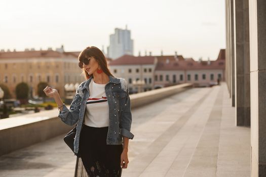 A young woman in a modish summer outfit is walking in the city street in the summer day