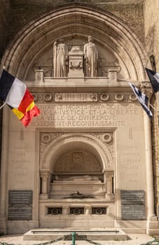 Dunkerque, France - September 16, 2018: Closeup of World wars memorial with flags at base of Belfry of Dunkirk. Fifty shades of brown broken by colors of flags.