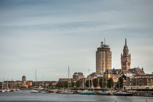 Dunkerque, France - September 16, 2018: Old Port with sailing yachts and three towers, LTR: Leughenaer historic lightower, condominiums, Belfry of Dunkirk town hall under light blue skay.