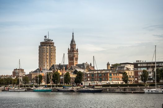 Dunkerque, France - September 16, 2018: Old Port with sailing yachts and two towers: condominiums, Belfry of Dunkirk town hall under light blue sky. Red brick other buildings.