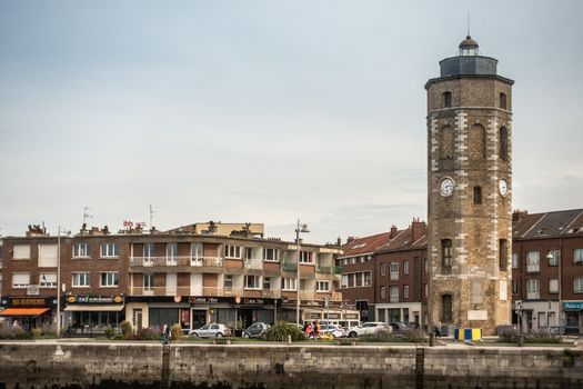 Dunkerque, France - September 16, 2018: Leughenaer brick Clock tower and historic lighthouse on Minck Square at old port of Dunkirk. Street scene with people and cars. Light blue sky.