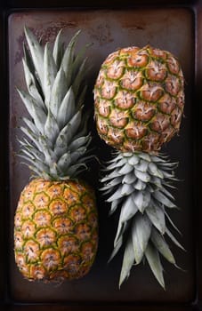 High angle view of two whole fresh ripe pineapples on a metal baking sheet.