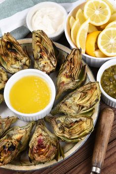 Vertical high angle shot of a plate full of grilled artichokes with butter, mayonnaise and lemons