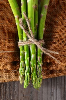 Closeup of Asparagus bunches tied with twine on a burlap and wood background. Overhead shot in vertical format.